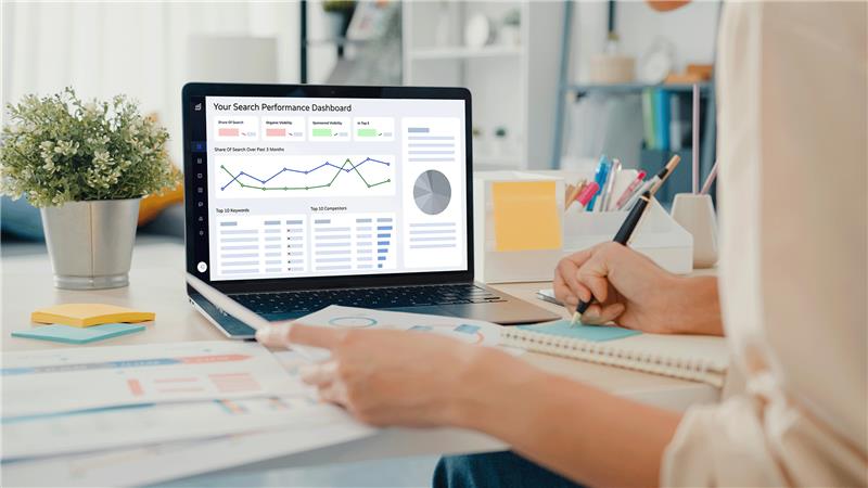 A person reviews a search performance dashboard on a laptop, taking notes in a notebook with colorful sticky notes nearby.